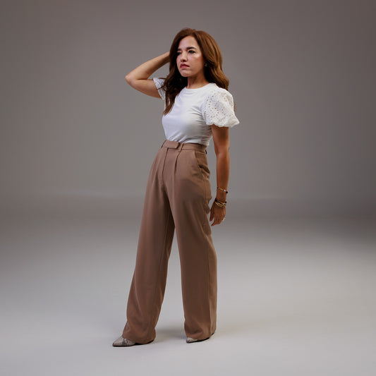 Woman wearing a white top and brown pants against a gray background