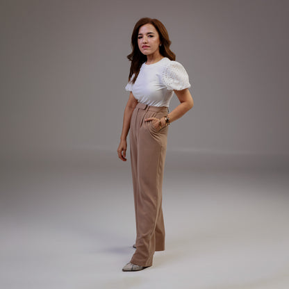 Woman wearing a white top and beige pants against a plain background
